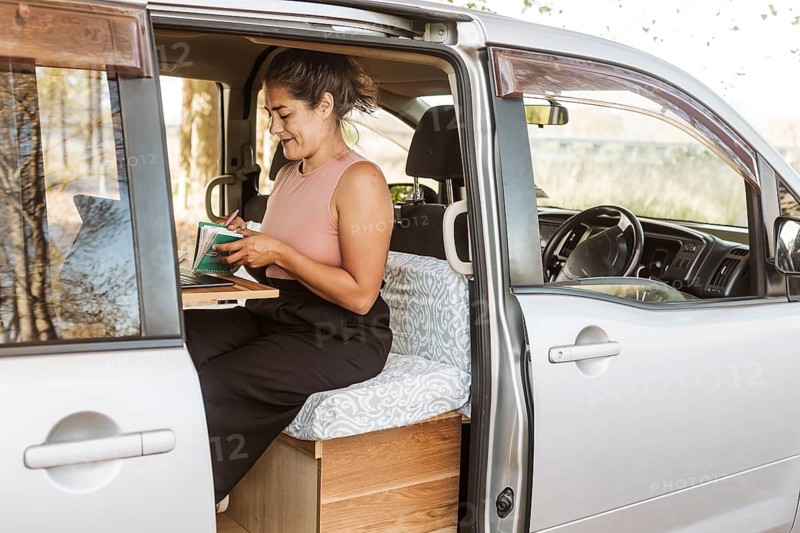 A woman works inside her van, surrounded by the golden hues of autumn in New Zealand. Her mobile workspace reflects the essence of remote work and adventure