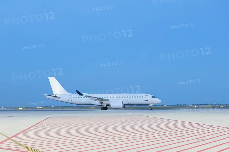 A sleek white airplane sits on a vast airport runway, capturing the tranquility of travel moments before takeoff. The soft sunset glow highlights the scene's serene ambiance