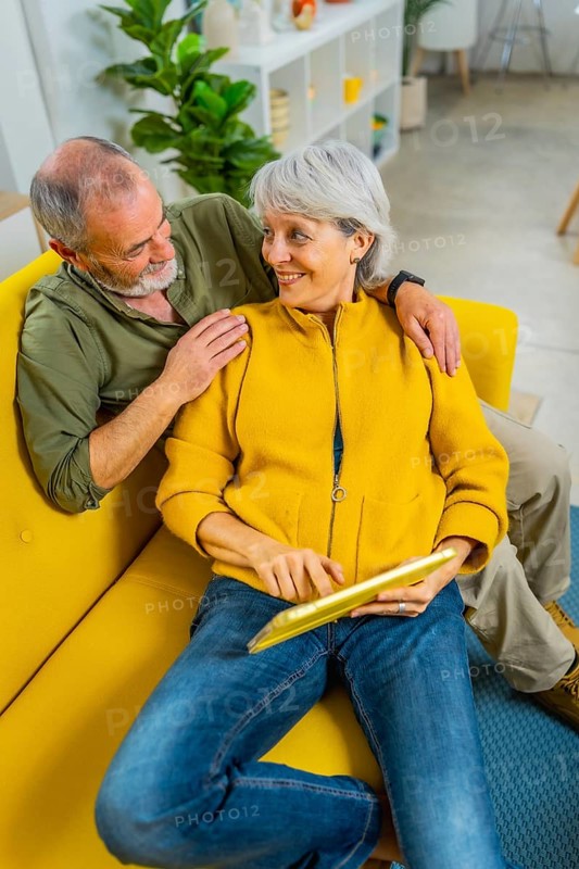 Vertical photo of a relaxed senior couple lying on the sofa using digital tablet