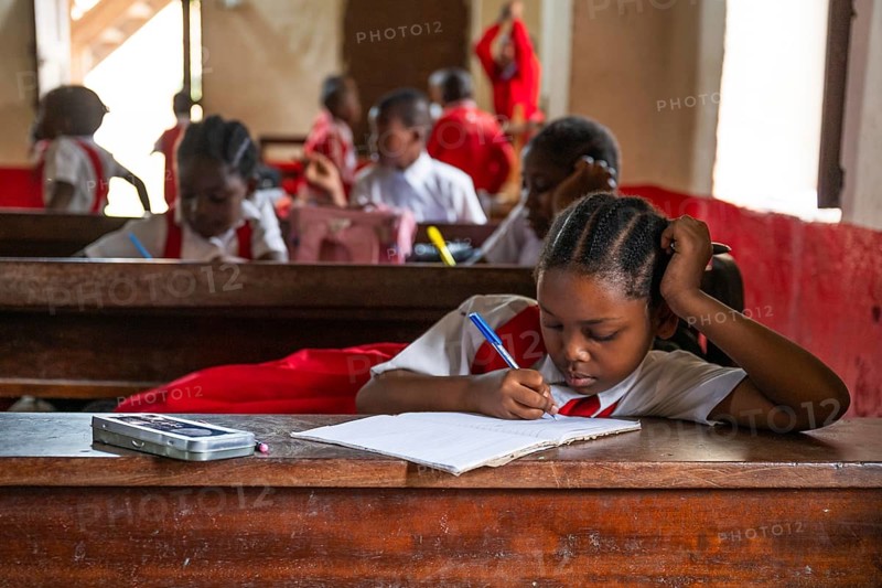 MICHAMVI KAE, ZANZIBAR - OCTOBER 16, 2025: Close up of a young African girl in a school uniform concentrating and writing in her notebook during a lesson in a Zanzibar classroom
