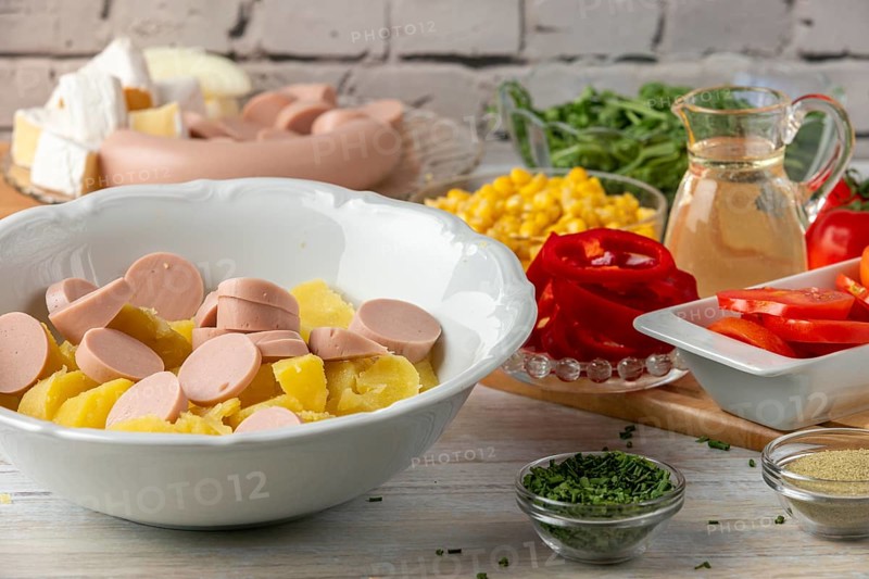 Potatoes and sausage in a bowl surrounded by other ingredients such as peppers, corn, cheese and arugula
