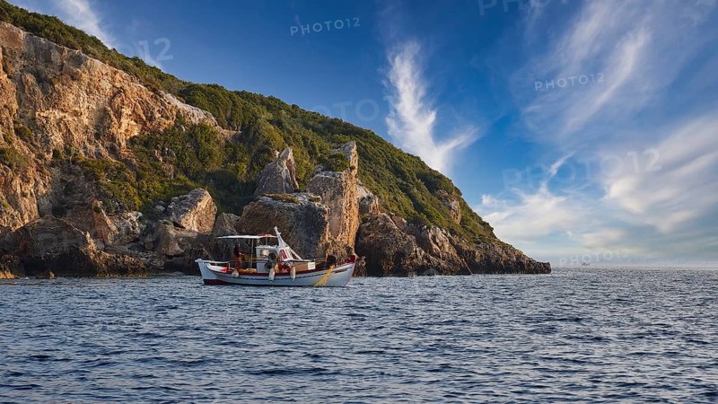 A boat moves along the coast with distinctive cliffs under a sky full of dramatic clouds, morning light, Navarino Bay, Pylos, Peloponnese, Greece