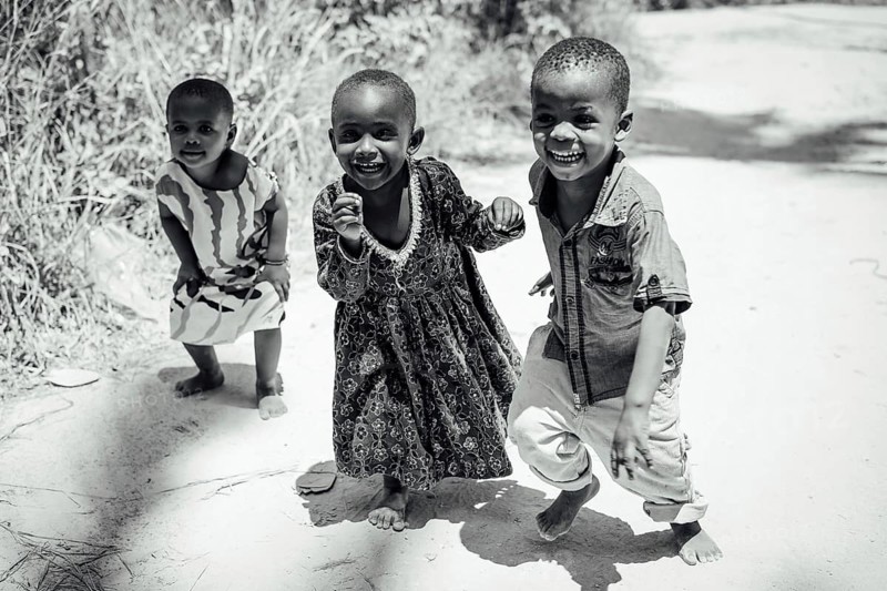 MICHAMVI KAE, ZANZIBAR - OCTOBER 17, 2025: Group of happy and laughing African children playing and running on a sunny sandy path in a rural area