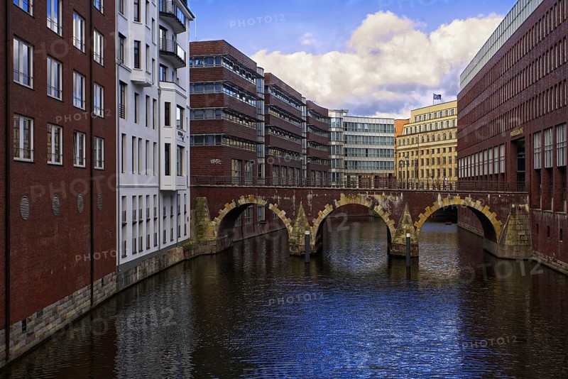 City view with Bleichenfleet canal and old stone bridge surrounded by modern brick buildings, blue sky, Hamburg, Germany