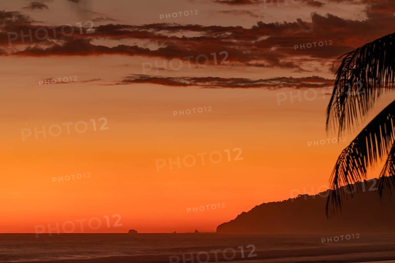 After sunset, the deep red sky glows above palms and ocean spray with views of Corcovado National Park. Costa Rica