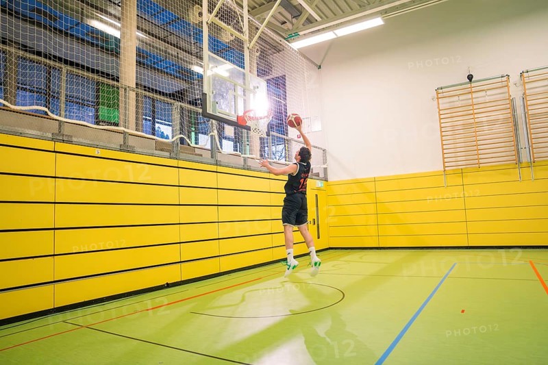 A player jumps up to throw the ball into the basket in a yellow gym, basketball TSV Calw, Germany