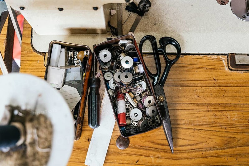 A collection of sewing tools and supplies, including scissors, spools, and a screwdriver, laid out on a wooden work surface, highlighting a well used workspace in Asia