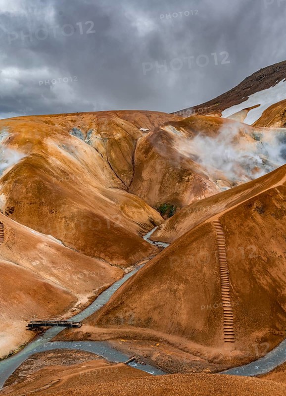 Bridge over steaming stream between colourful rhyolite mountains with snowfields, Hveradalir geothermal area, Kerlingarfjöll, Icelandic highlands, Iceland