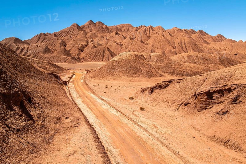 Breathtaking view of a rugged desert landscape featuring a winding dirt road, surrounded by hilly terrain under a vivid blue sky in the argentine Puna. Perfect for travel or nature themes
