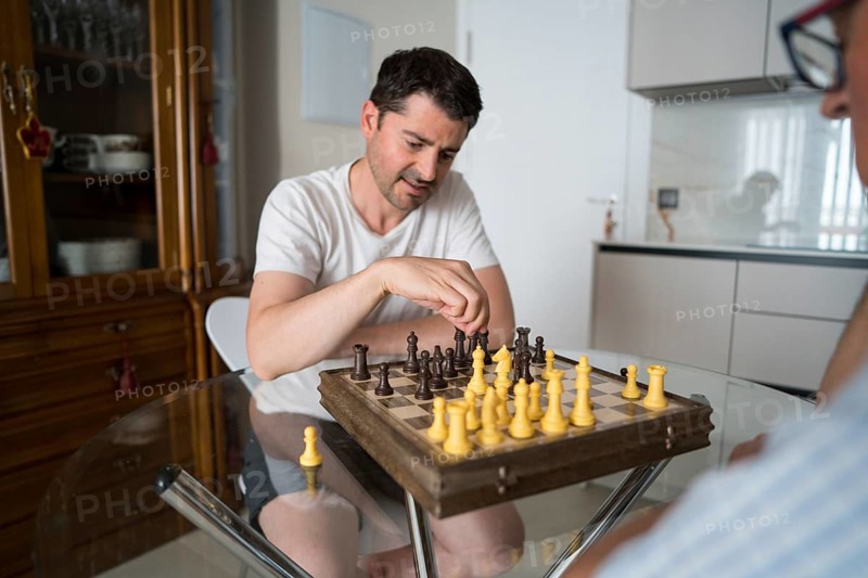 A cropped unrecognizable father and son enjoying a focused game of chess at home, sharing quality time and fostering intergenerational bonding through strategic play and conversation