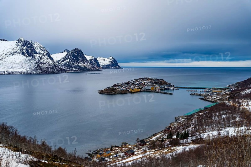 Husøy island in the fjord, snow-capped mountains behind it, Senja island, Troms, Norway
