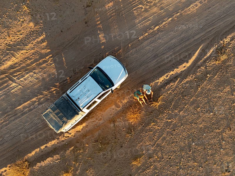 Top Down View, Two travelers sitting next to off-road car on dust road in the desert, aerial view, Erongo, Damaraland, Namibia
