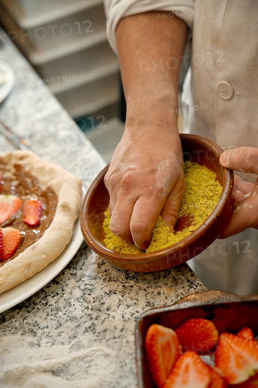 Cropped unrecognizable chef's hand sprinkling toppings on a gourmet pizza with ingredients on a kitchen counter