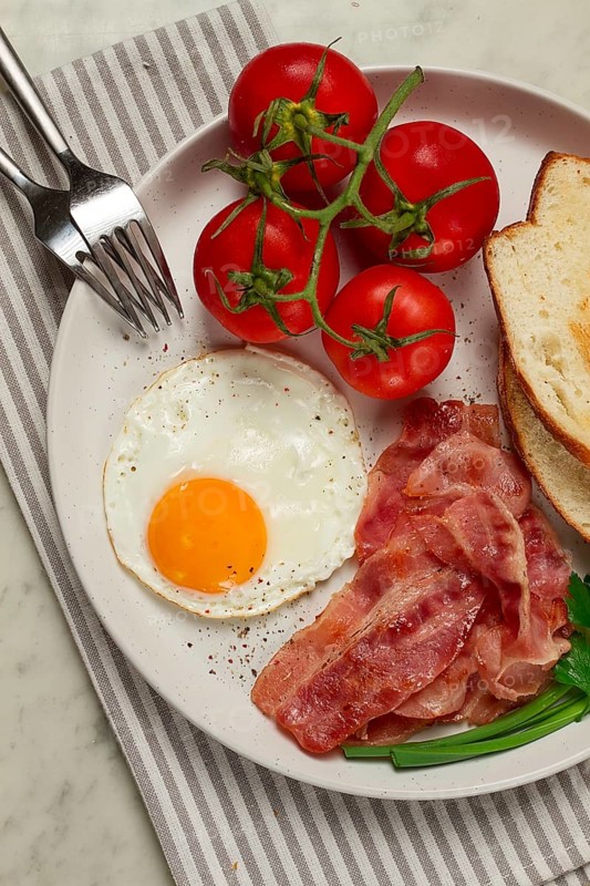 Breakfast, fried egg, bacon and bread, with cherry, on a light background, homemade, no people