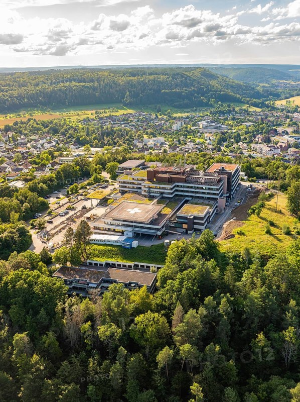 A large building surrounded by densely wooded hills and a cityscape, taken from the air under a cloudy sky, Hospital, Nagold, Black Forest, Germany