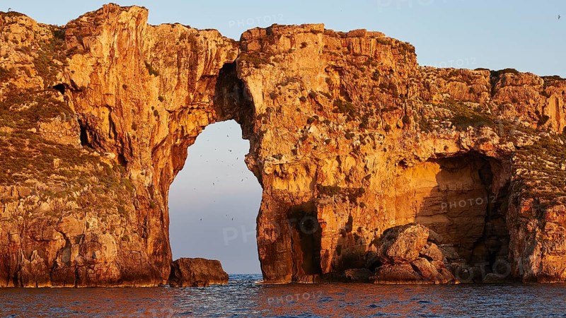 Impressive rock formation with an arch in the sea at sunrise, morning light, Tsichli Babas islet, Navarino Bay, Pylos, Peloponnese, Greece