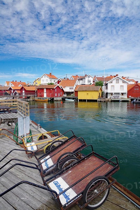 Wooden houses on the water with boats, blue sky with clouds shows a peaceful harbour atmosphere, transport carts, car-free island, archipelago, Gullholmen, Västra Götalands län, Sweden