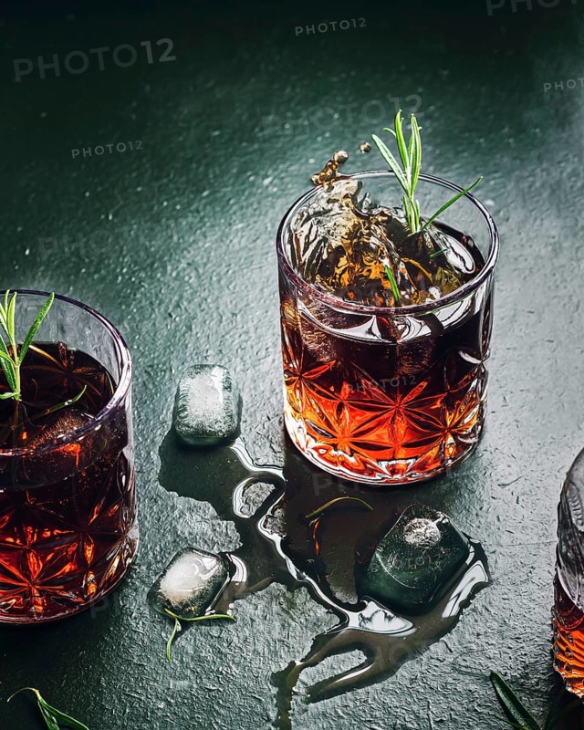 A dramatic scene of whiskey splashing in a glass garnished with rosemary, surrounded by scattered ice cubes on a dark textured surface, creating a moody atmosphere