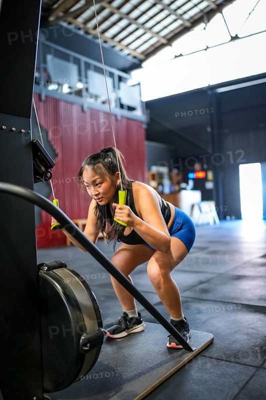 Vertical photo with full length and copy space of a Chinese strong sportive woman pulling weights in a lat machine in a gym