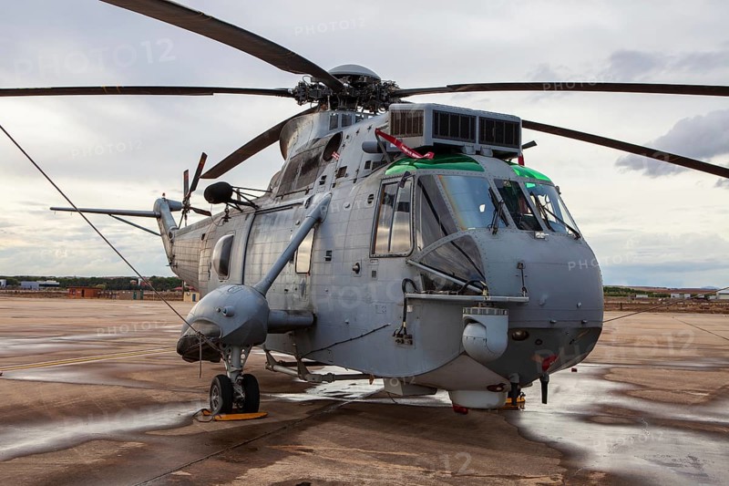 A large military helicopter is parked on the wet tarmac at Torrejon Air Base. The aircraft's powerful rotor blades and rugged design highlight its tactical and transport capabilities