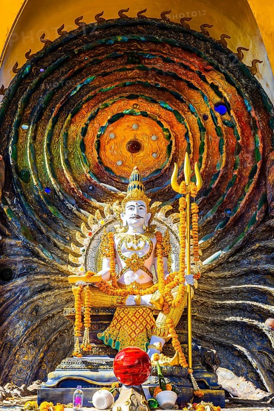 Hindu deity Shiva holding a trident, offerings in the foreground, a cosmic symbol in the back, Buddhist temple complex Wat Phra That Sorn Kaew, Phetchabun province, Thailand
