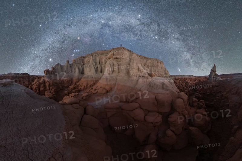 Captivating night sky full of stars, illuminating Goblin Valley State Park in Utah, highlighting the rugged desert landscape against a brilliant Milky Way backdrop with unrecognizable person silhouette standing on top of the mountain