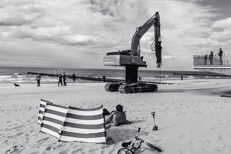 TRZESACZ, POLAND - MAY 1, 2018: The excavator for driving piles goes through the beach with tourists