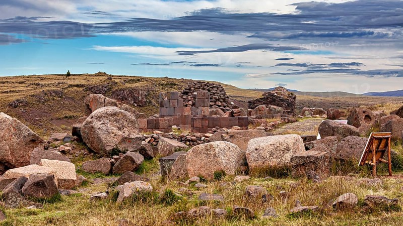Ruins of stone blocks and large rocks in a grassy landscape under a blue sky, The Chullpas of Sillustani near Puno in Peru