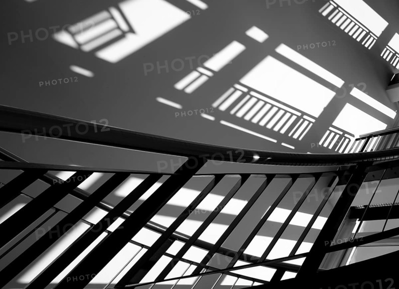 A black stair railing casts shadows on a white wall in the stairwell, Berlin