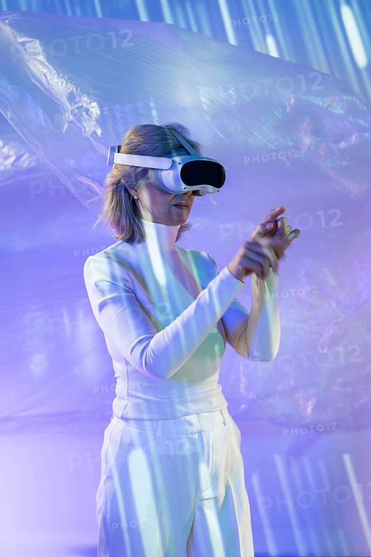 An elderly Asian woman engaging with the metaverse, wearing a VR headset. She navigates an immersive digital environment, symbolizing technology's reach across generations