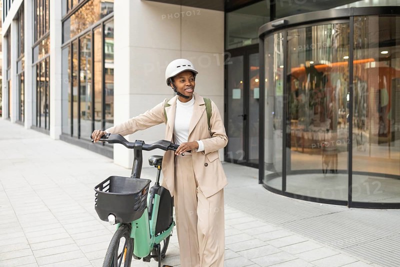 Black woman in a trendy outfit with a helmet, walking her bicycle in a modern cityscape Perfect blend of style and urban life, showcasing active lifestyle