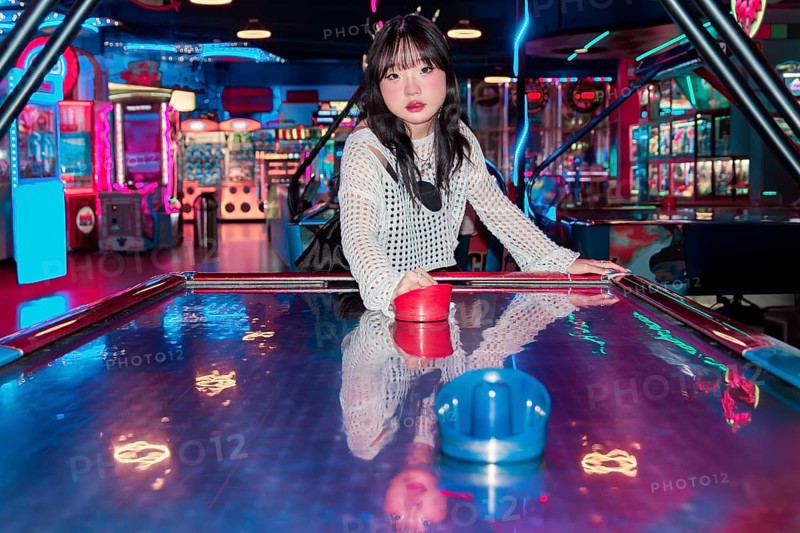 An Asian Gen Z girl having fun in an arcade, surrounded by vibrant neon lights and colorful games Her enjoyment and youthful energy fill the entertainment atmosphere