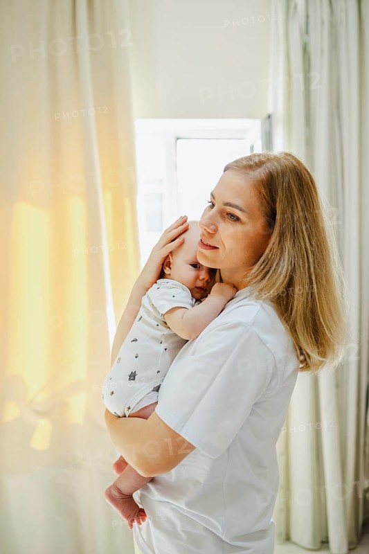 A serene scene of a mother gently holding her baby close, bathed in soft sunlight streaming through curtains, capturing a tender moment of affection and warmth