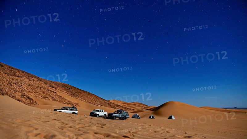 Night shot of a desert camp with tents and cars under a starry sky, adventure camping with off-road vehicles in the Sahara desert in Algeria
