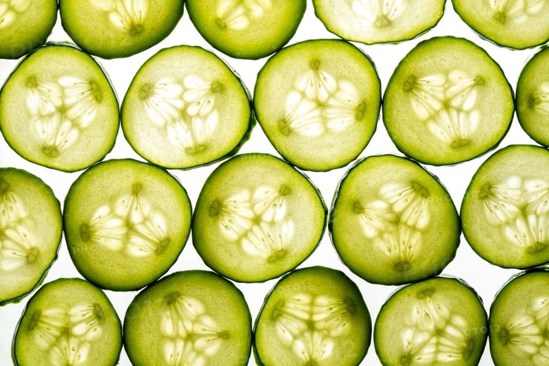 A close up image of green cucumber slices arranged in a seamless pattern. The fresh and vibrant slices display intricate details, showcasing their crisp texture and natural beauty