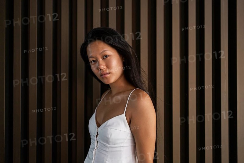 A Chinese woman in a summer outfit stands against a city backdrop, exuding confidence. The warm tones highlight the season, contrasting with the urban environment