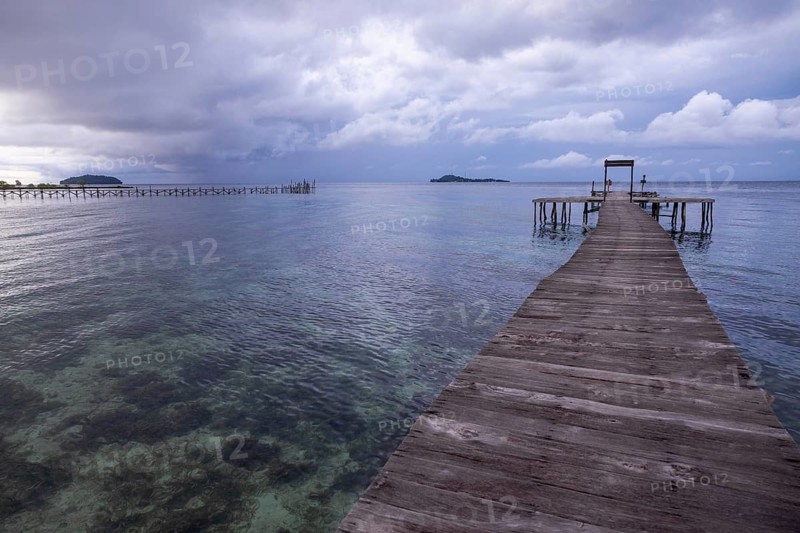 A serene view from a wooden pier on Waigeo Island, Indonesia. Cloudy skies enhance the tranquil atmosphere