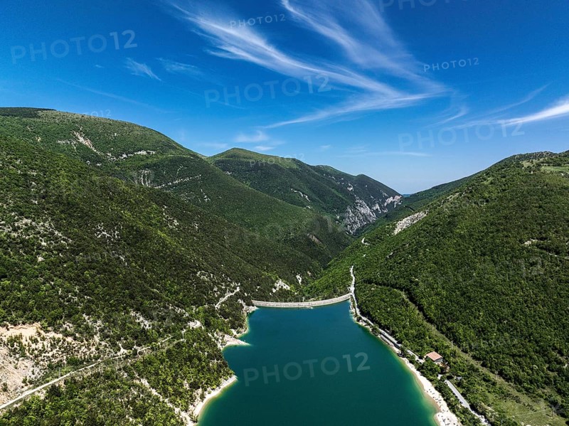 Serene beauty of Lago di Fiastra in Italy. This aerial shot captures the clear blue water surrounded by lush green hills under a vibrant sky