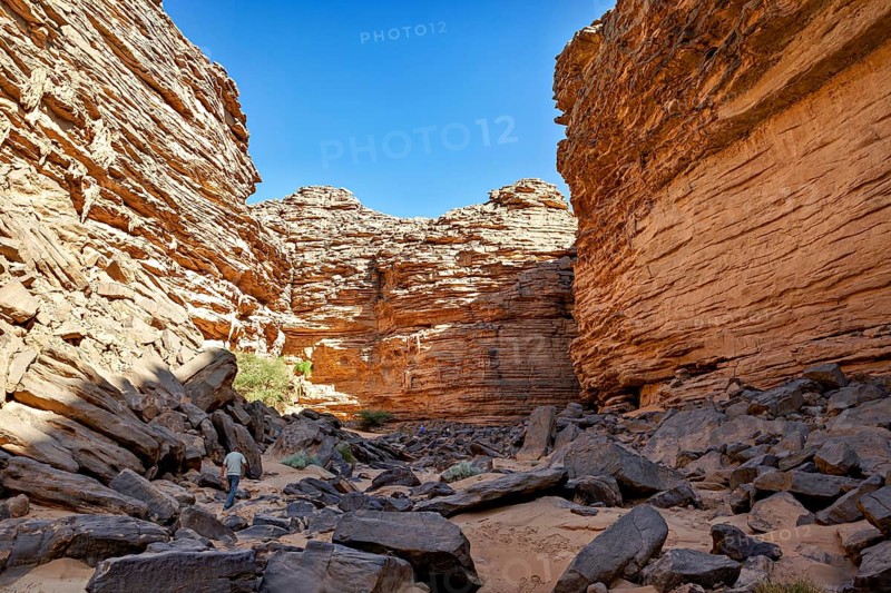 Deep gorge with jagged rock faces and a wandering man in an arid environment, rocky gorge in the desert landscape of the Sahara in Algeria