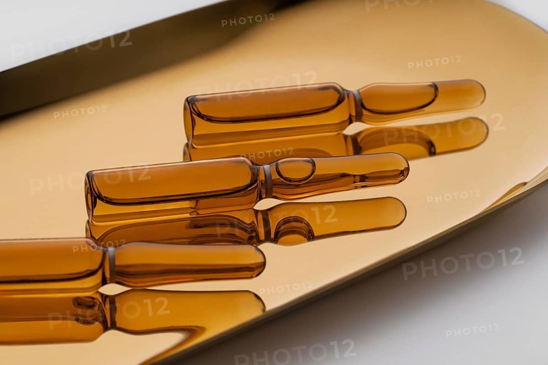 Transparent glass ampoules filled with golden anti-aging serum, elegantly displayed on a reflective beige surface