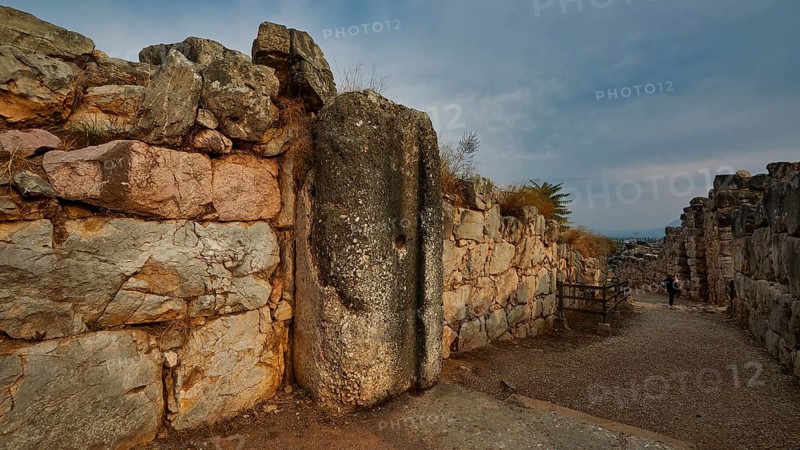 Cyclopean wall, gate, old paved path between high stone walls under a cloudy sky, Tiryns, ancient city in Argolis, Mycenaean, Peloponnese, Greece