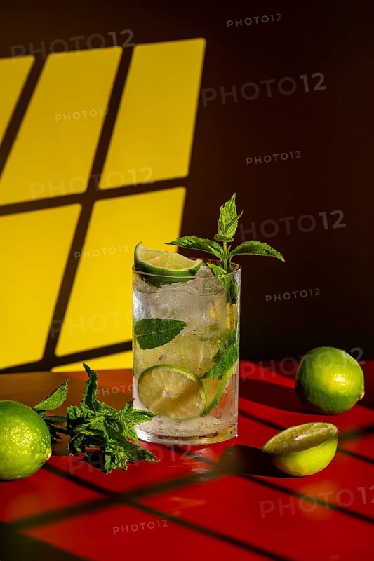 A refreshing classic mojito garnished with lime and mint, set against a bold red tabletop with a warm yellow background. Perfect for a summer cocktail-themed visual