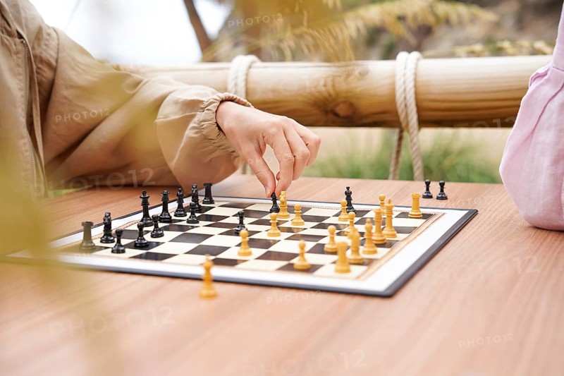 Hands move chess pieces on a board placed on a wooden table outdoors The scene conveys a relaxed and strategic game in a natural setting with family