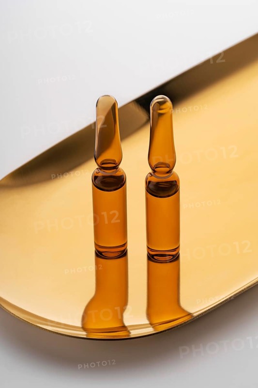 Three brown glass ampoules filled with anti-aging serum, elegantly presented on a reflective golden tray, symbolizing luxury skincare