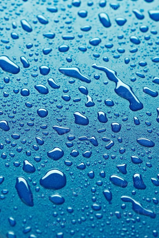 Close up image of water droplets on a smooth blue surface. The droplets vary in size, creating a refreshing, abstract pattern against a vibrant background