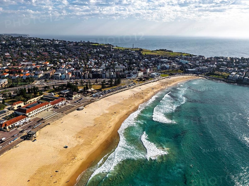 Aerial view of a beautiful coastal town with sandy beach, blue ocean, and residential area in Sidney, Australia. Waves gently lap the shore, creating a serene and inviting atmosphere