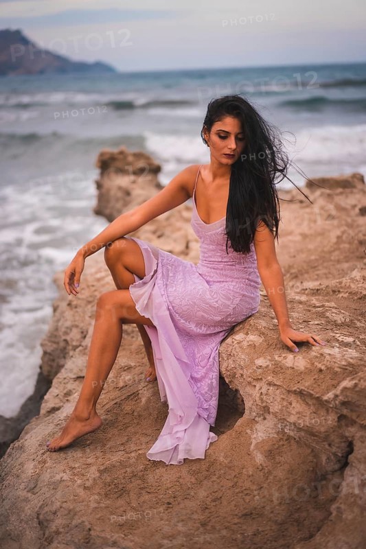 Posing of a young brunette Caucasian in a pink dress, on the beach having fun by the sea