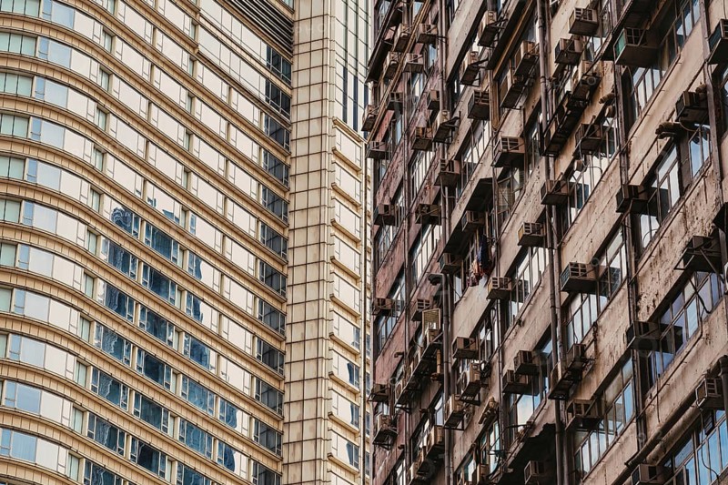 This image captures a striking contrast between sleek, modern architecture and an old residential building in Hong Kong, highlighting the diverse urban landscape
