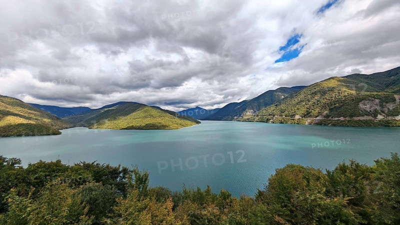 Calm lake surrounded by wooded mountains under partly cloudy sky, Georgia