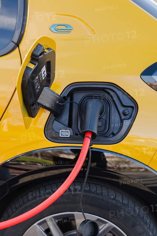 Close-up of an electric car charging with a vivid red cable at a station. The yellow vehicle's intricate charging port is visible, emphasizing modern eco-friendly technology